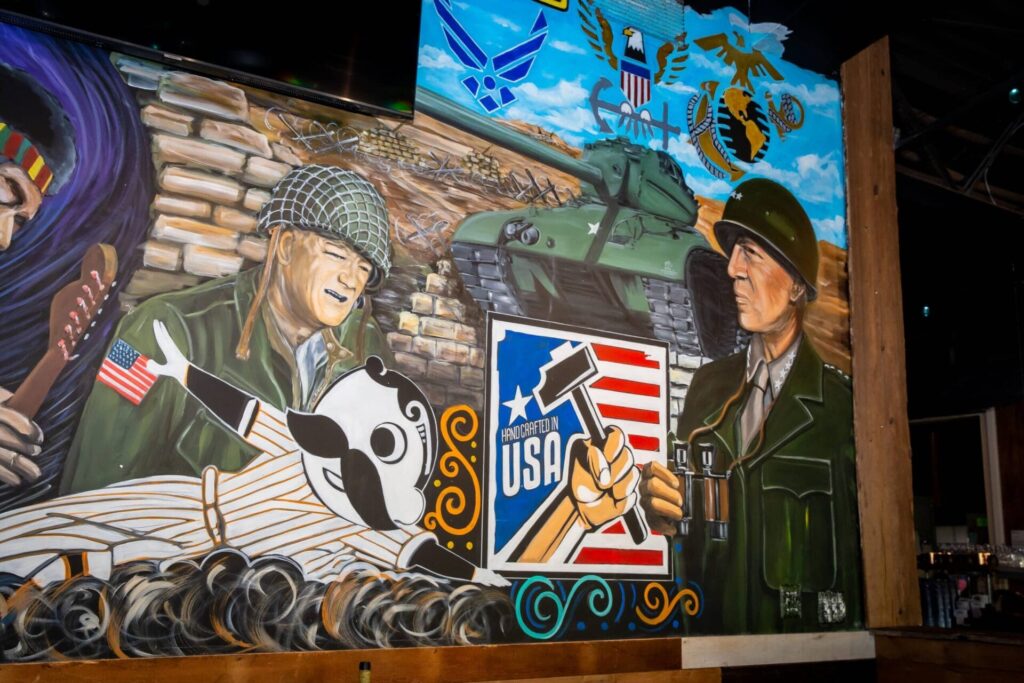 A colorful mural featuring two World War II soldiers, one holding a guitar and the other binoculars, with a tank, USA logos, and military insignia in the background at the best restaurant in Woodbine MD.